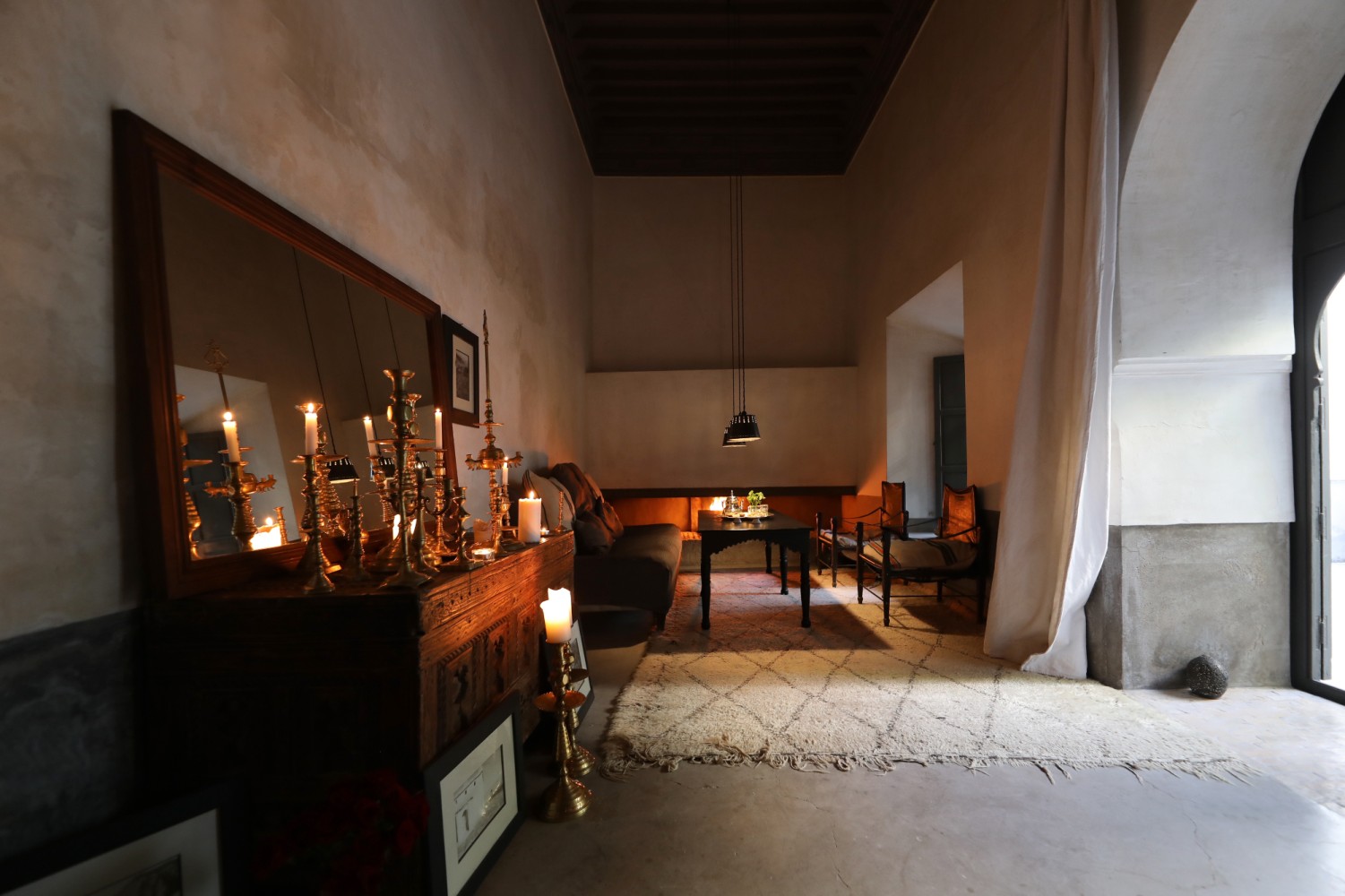 The riad's grand lounge as day fades, brass candlesticks lit beside the fireplace