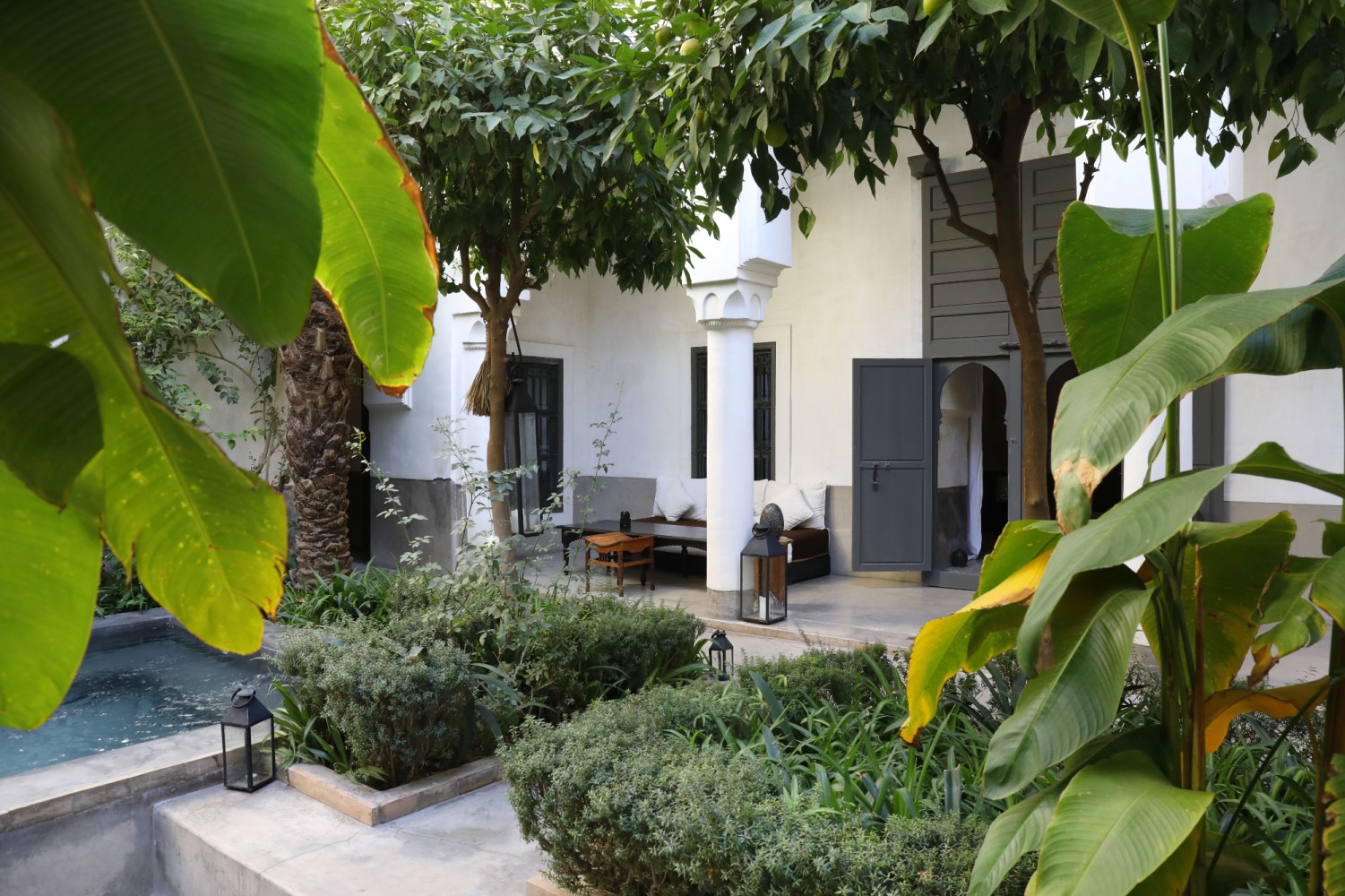 Le patio du riad — colonne blanche, banquettes et lanternes au bord du bassin