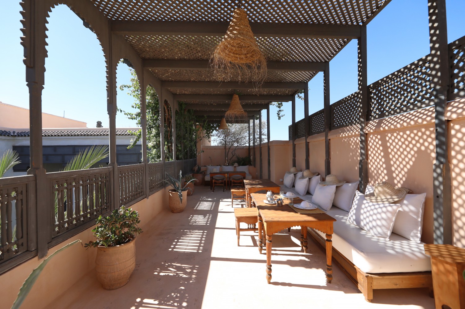 The rooftop pergola — banquettes, white cushions and straw hats