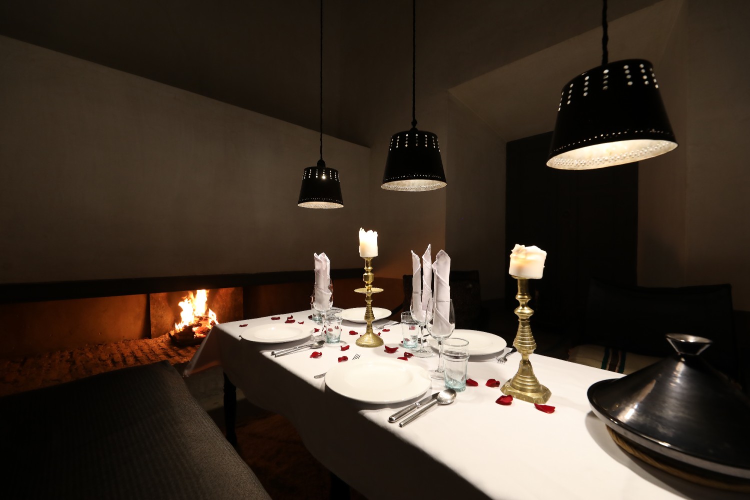 The dinner table dressed in white before the fireplace: brass candlesticks, rose petals, a silver tagine